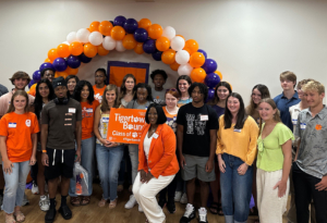 group of new students posing in front of an orange, white and purple balloon arch